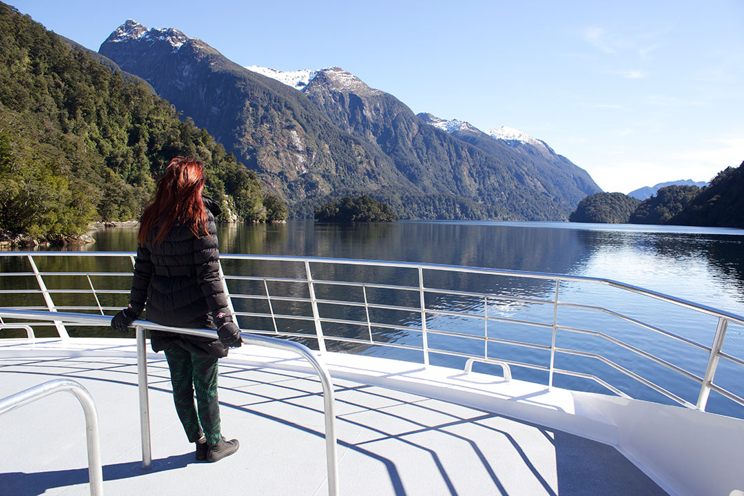 Standing on the back of the Catamaran, looking out over the peaceful, calm waters of Doubtful Sound with the snow-capped mountains and fjords in the background in New Zealand