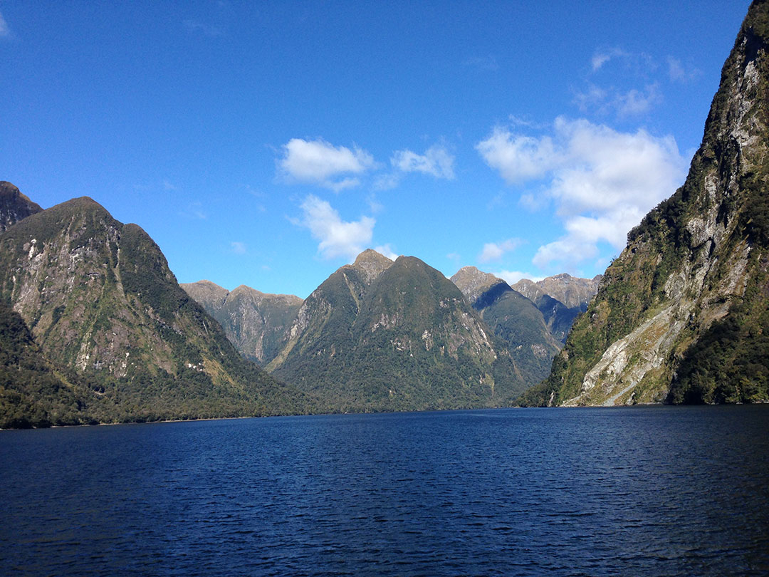 View from the back of the Catamaran, looking out over the peaceful, calm waters of Doubtful Sound with the snow-capped mountains and fjords in the background in New Zealand