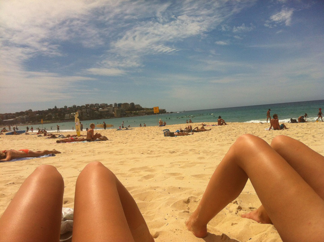 Tanned legs with feet in the sand, lying down on Bondi Beach overlooking the ocean
