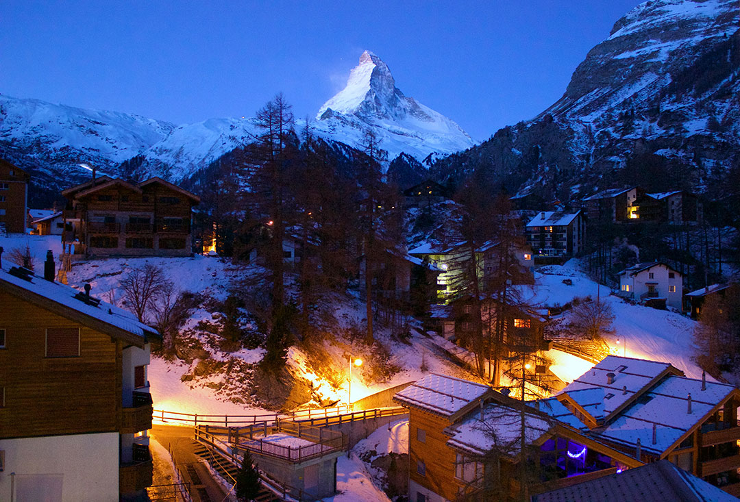 View of the Matterhorn at night with low-rise hotels lit up in the foreground with snow-covered ground