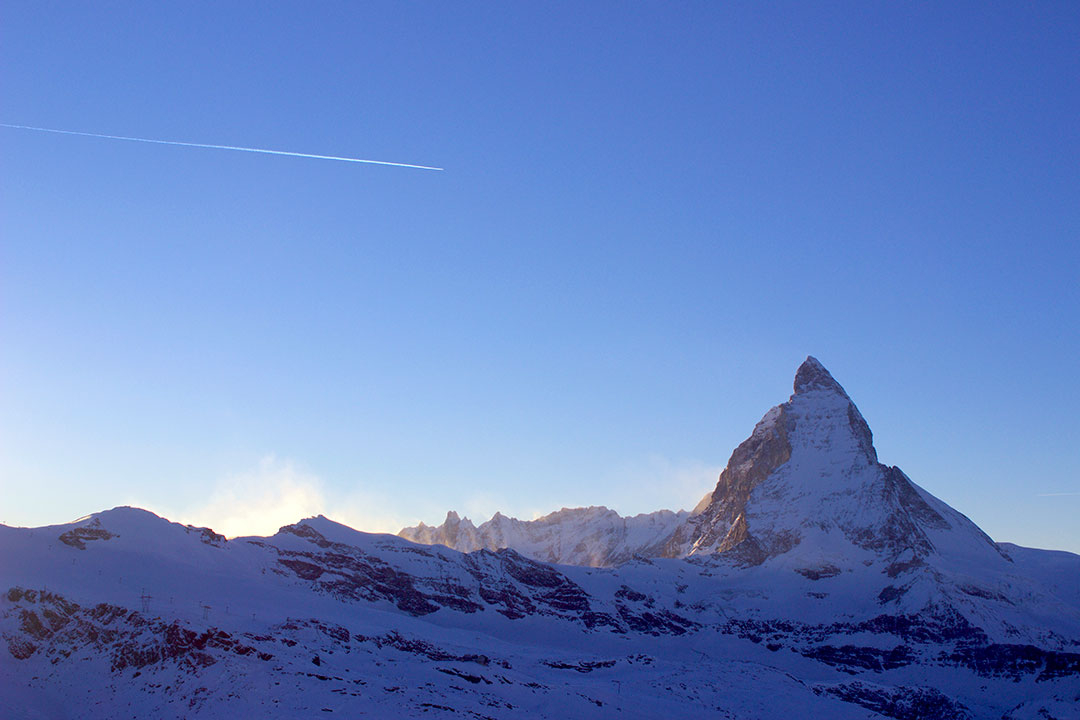 A plane flies overhead with the snow-covered Matterhorn in the distance while snow sledding