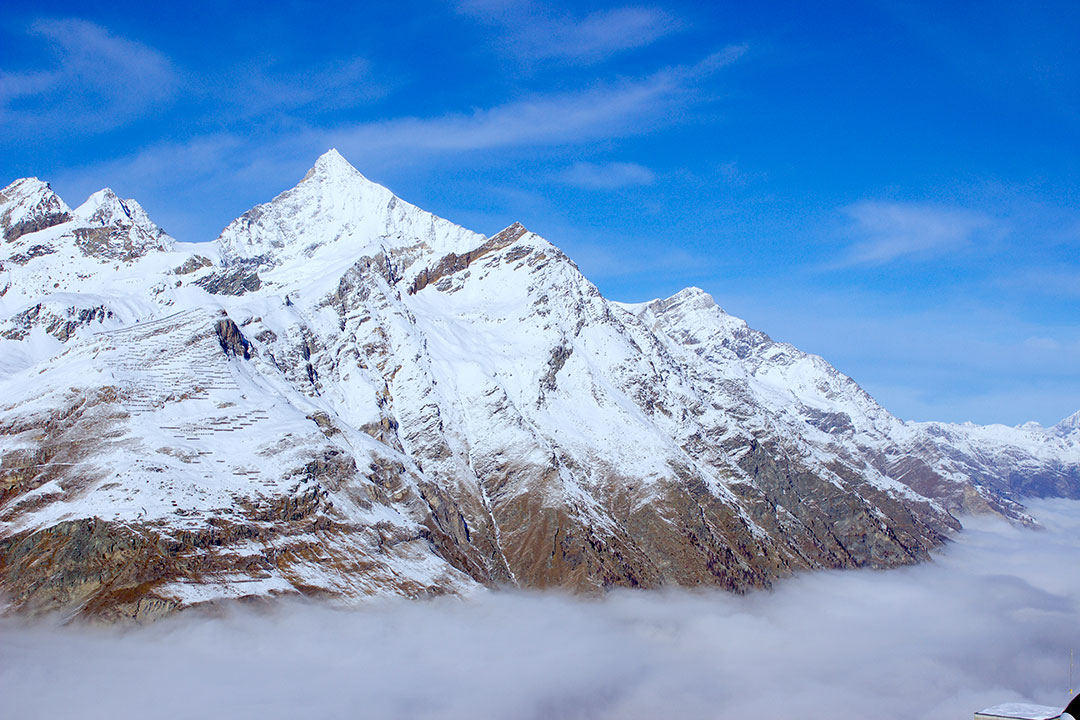 View from the train while looking down over the snow-covered Swiss Alps on a blue sky winter day above the clouds