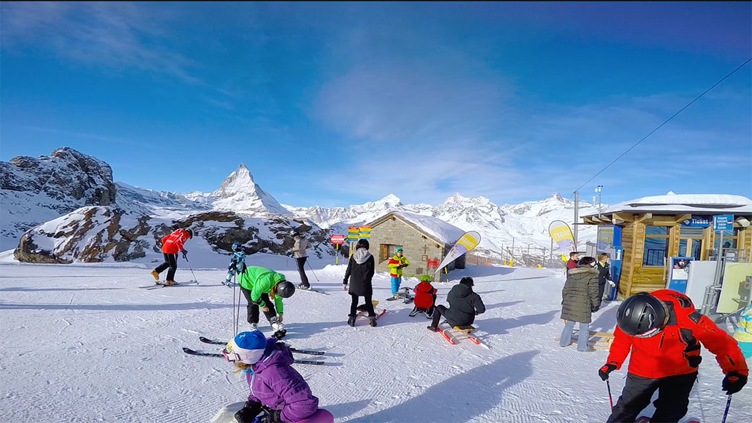 Colourful skiers and snow sledders standing ready to go down the mountain with the Matterhorn in the background against a blue sky winter day in Switzerland