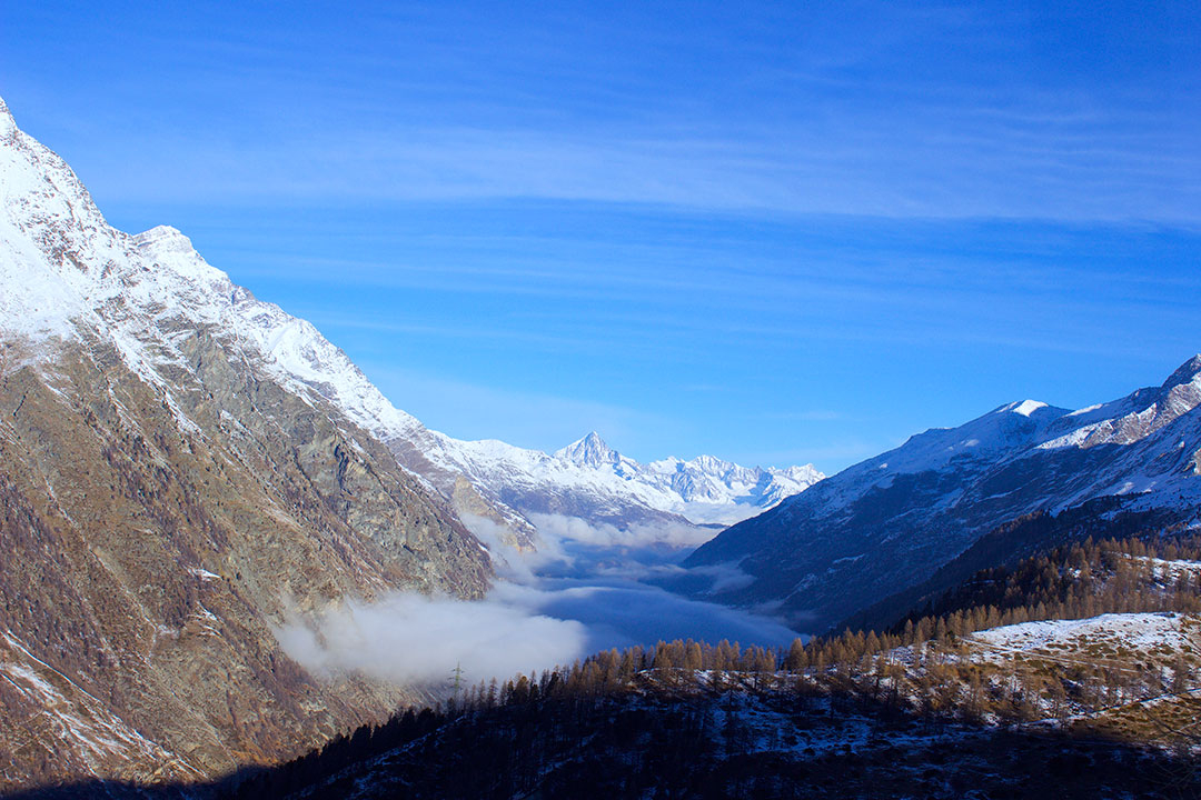 View from the train while looking down over the snow-covered Swiss Alps on a blue sky winter day above the clouds