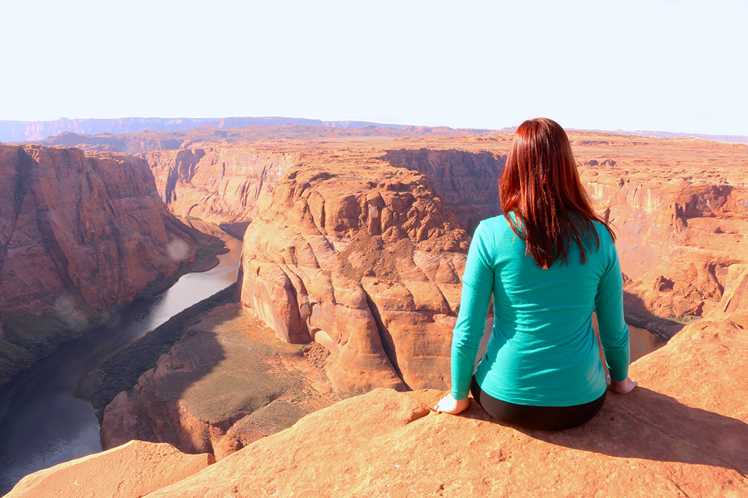 Me sitting on the cliff edge of Horse Shoe Bend overlooking the red rock and deep green water of the Colorado River