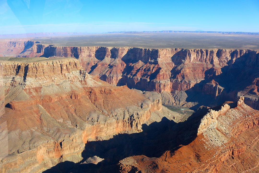 Beautiful helicopter views of the colourful red rock layers of the Grand Canyon on a brilliant blue sky day