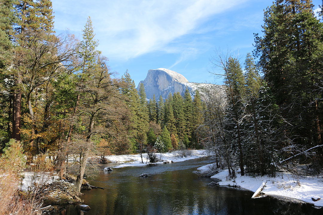 Perfect view of Half Dome looking proud over Yosemite National Park with a stream edged by snow on a perfect blue sky winter day