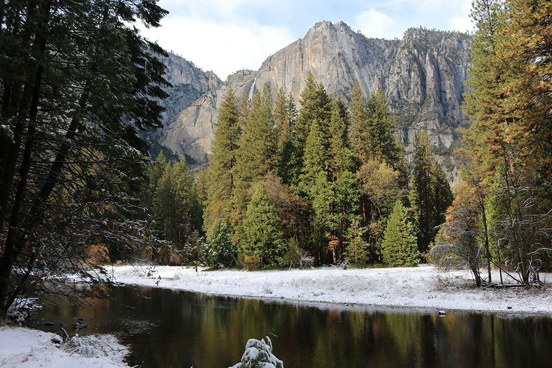 Beautiful view of Upper Yosemite Falls looking proud over Yosemite National Park with a stream edged by snow on a perfect blue sky winter day