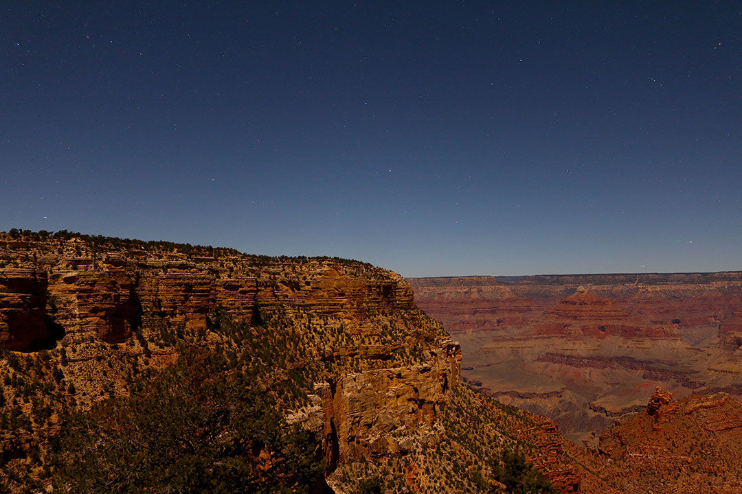 Warm red tones of the Grand Canyon at night with faint stars in the dark sky