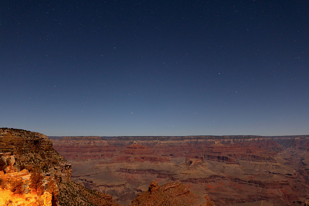 Warm red tones of the Grand Canyon at night with faint stars in the dark sky