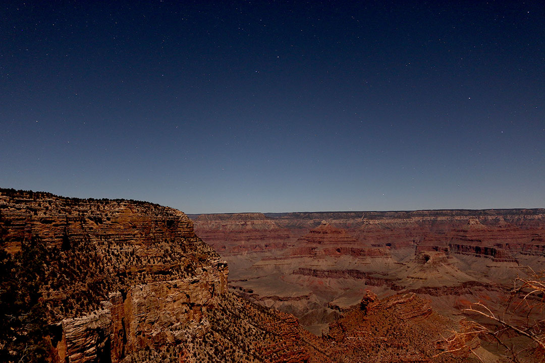 Warm red tones of the Grand Canyon at night with faint stars in the dark sky