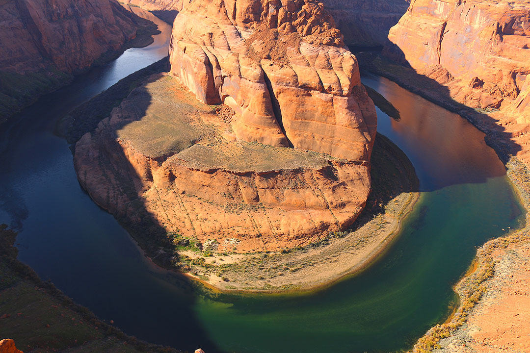 Deep green water in the Colorado River bending around the red rock of horse shoe bend