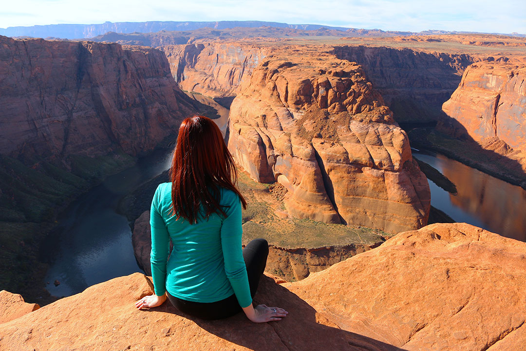 Me sitting on the cliff edge of Horse Shoe Bend overlooking the red rock and deep green water of the Colorado River