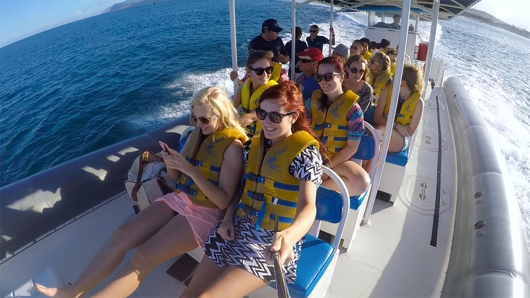 Group of friends on a fast catamaran smiling while wearing life jackets heading out on the ocean to the dolphins