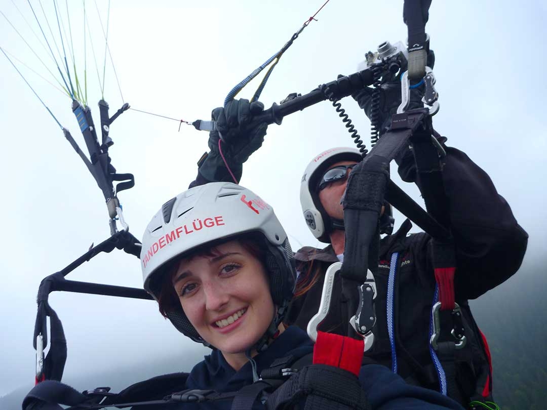 Me smiling while hanging from a parachute while paragliding through the clouds in Austria