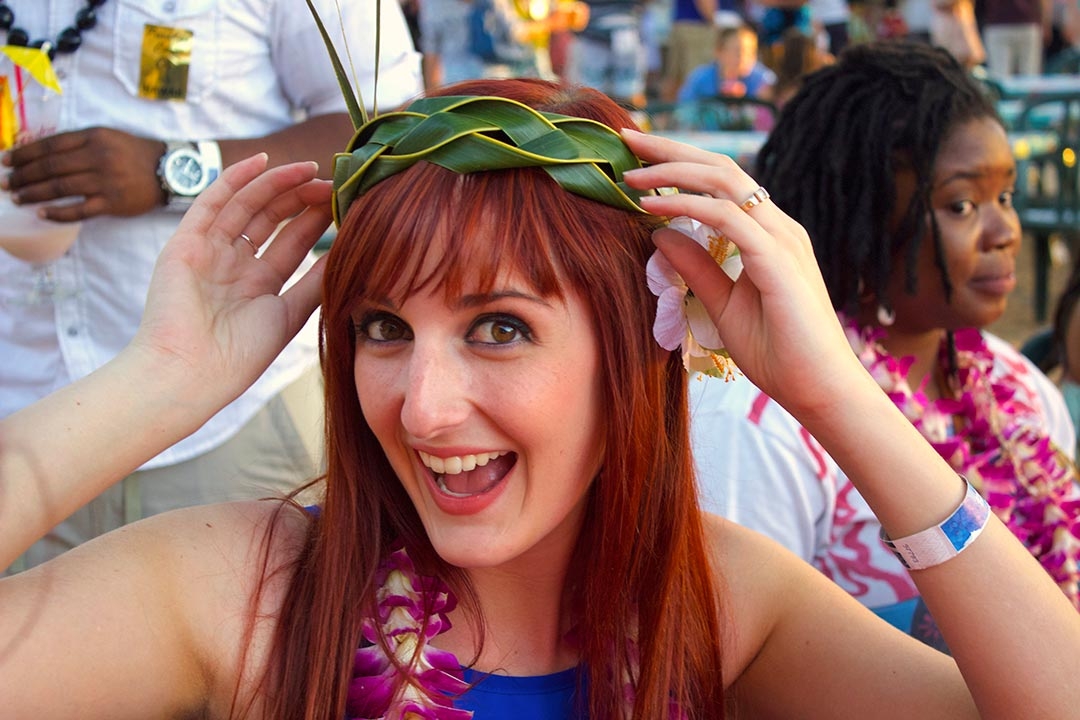 Me smiling cheerfully with my newly woven head dress on my head and a lady behind me giving me a strange look