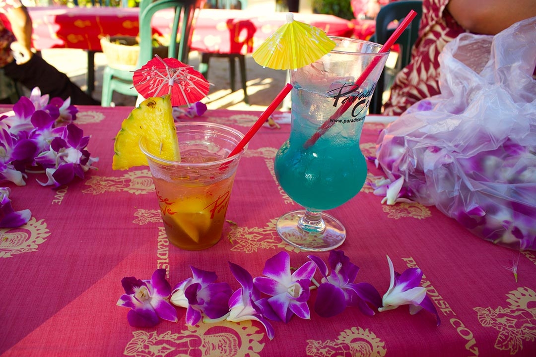 2 bright fun cocktails at the Luau with pineapple wedges and colourful mini umbrellas surrounded by flowers