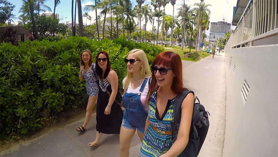 Group of 4 girl friends smiling and laughing while walking down a concrete path towards Waikiki Beach