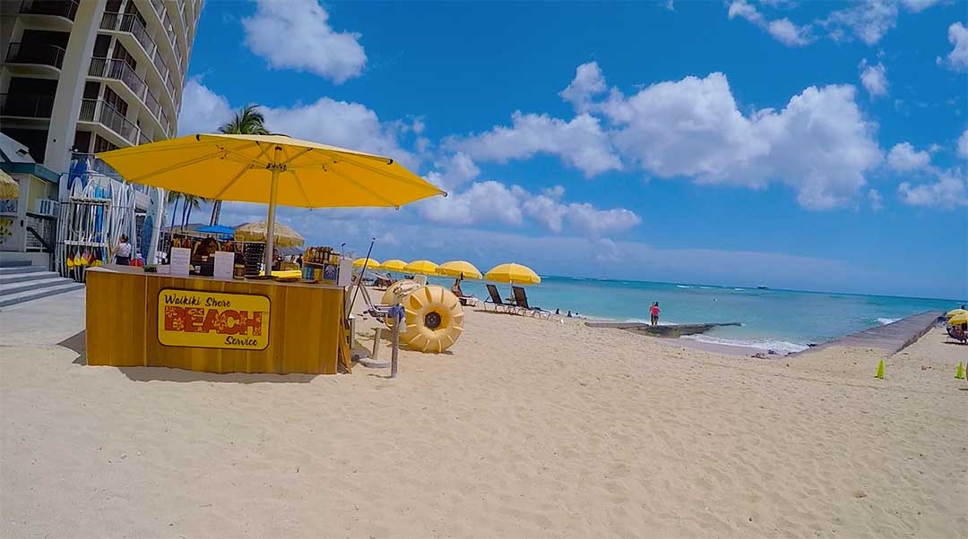 Yellow beach umbrellas line the waterfront at Waikiki beach on a perfect sunny Spring day