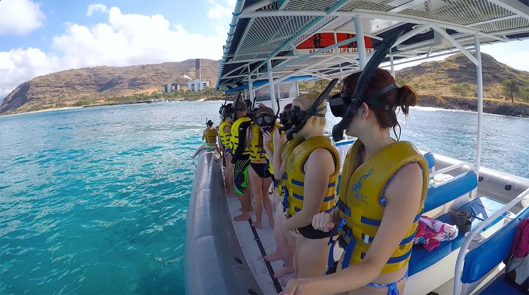 Group of friends ready on the side of the boat wearing lift vests, goggles and snorkels, ready to swim in the ocean near wild dolphins