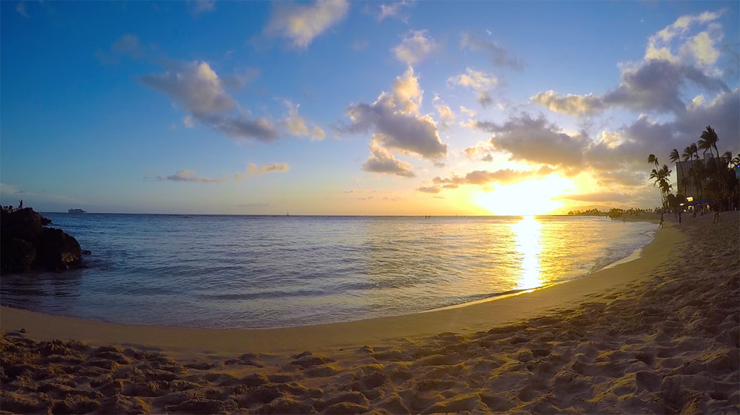 Sitting in the sand in front of the calm beach water, watching the beautiful sun set over the ocean on Waikiki Beach
