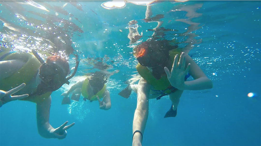 Friends smiling and waving under water while snorkelling looking for wild dolphins in Hawaii