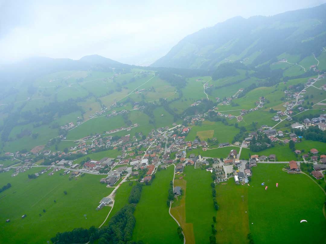 Amazing views of green rolling hills and little terracotta houses in the distance with clouds while paragliding Austria