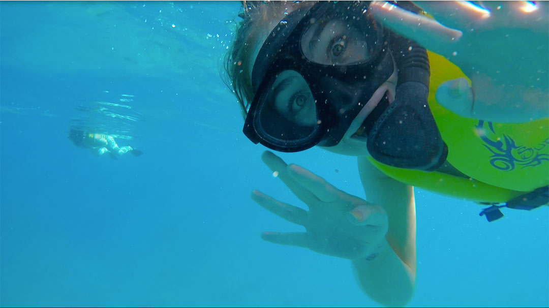 Friends smiling and waving under water while snorkelling looking for wild dolphins in Hawaii