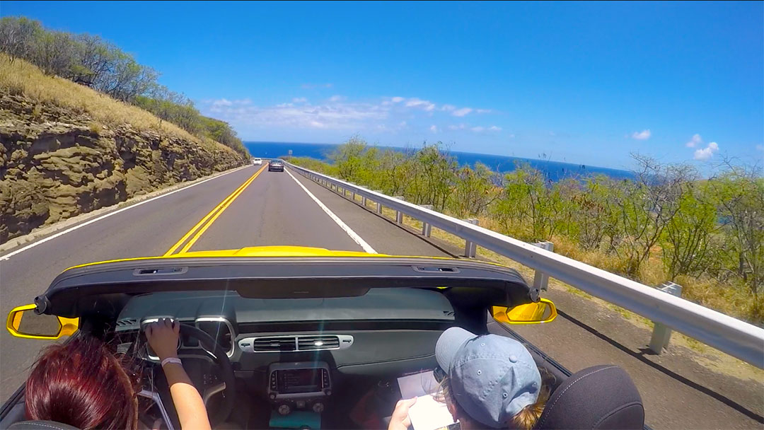 View from the back seat of the soft top Chevrolet Camaro with the top down while on a drive along the road beside the ocean on Oahu Hawaii