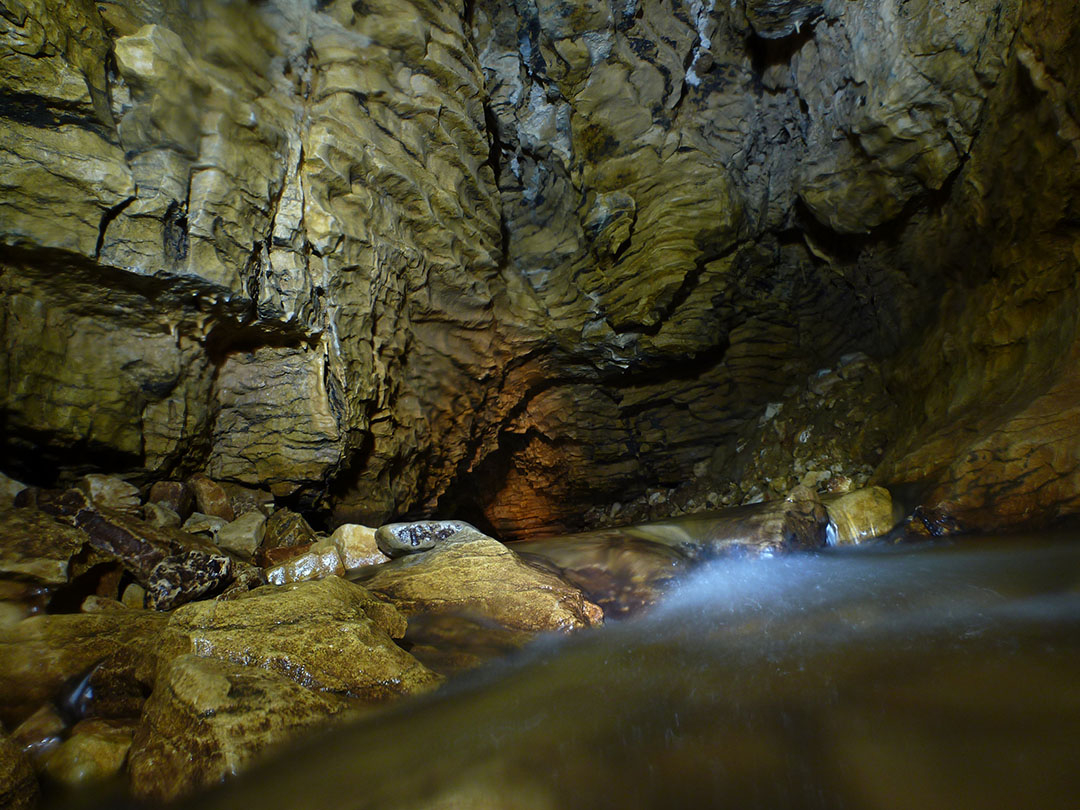 View inside the entrance to the cave with shallow water on the ground and wet rocky walls