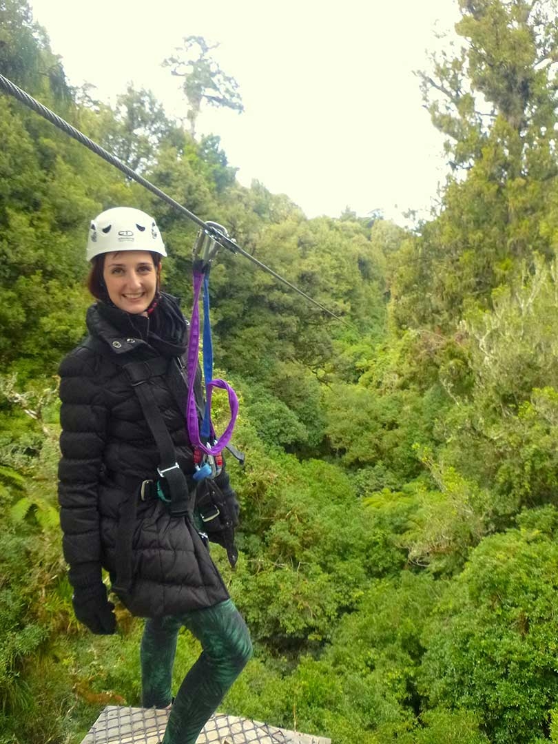 Me standing on the edge of a platform ready to jump off and zipline to the next platform wearing a helmet and harness in Rotorua, New Zealand