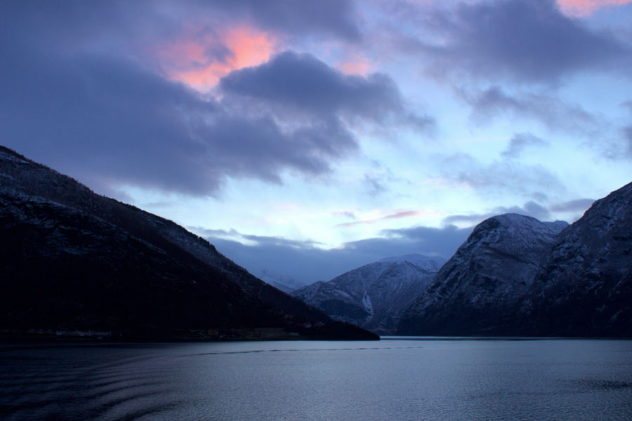 Beautiful view of Norwegian Fjords from the back of the ferry during sunset, with pretty pink clouds in the sky during winter in Norway