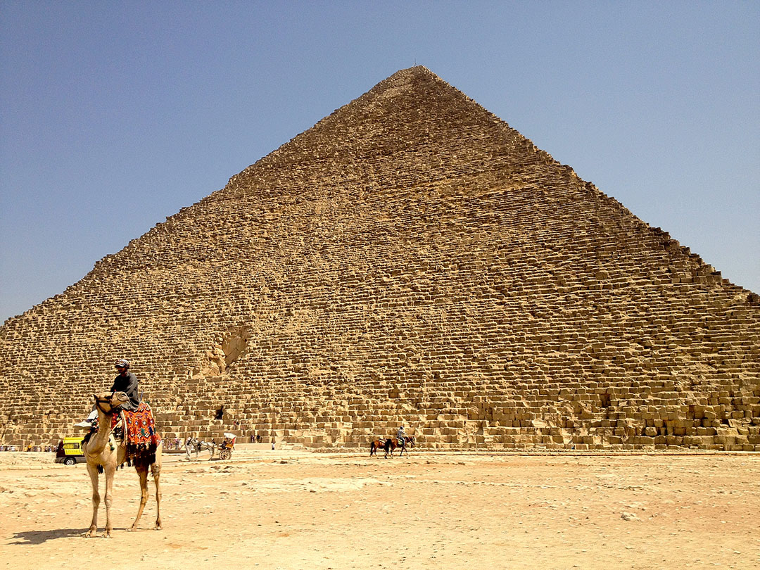 Man sitting on a camel out the front of the Grand Pyramid of Giza in Egypt on a hot summer day