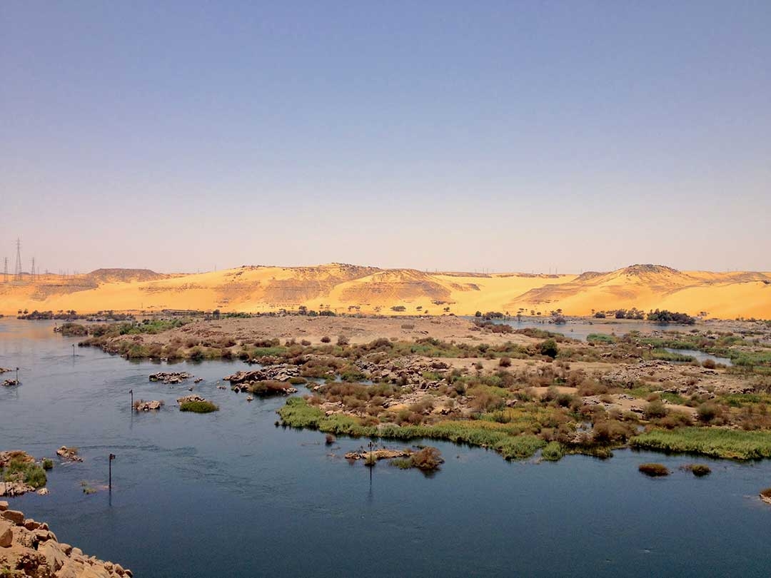 A small lake with moss covered rocks and sand dunes in the background in Giza, Egypt during Summer