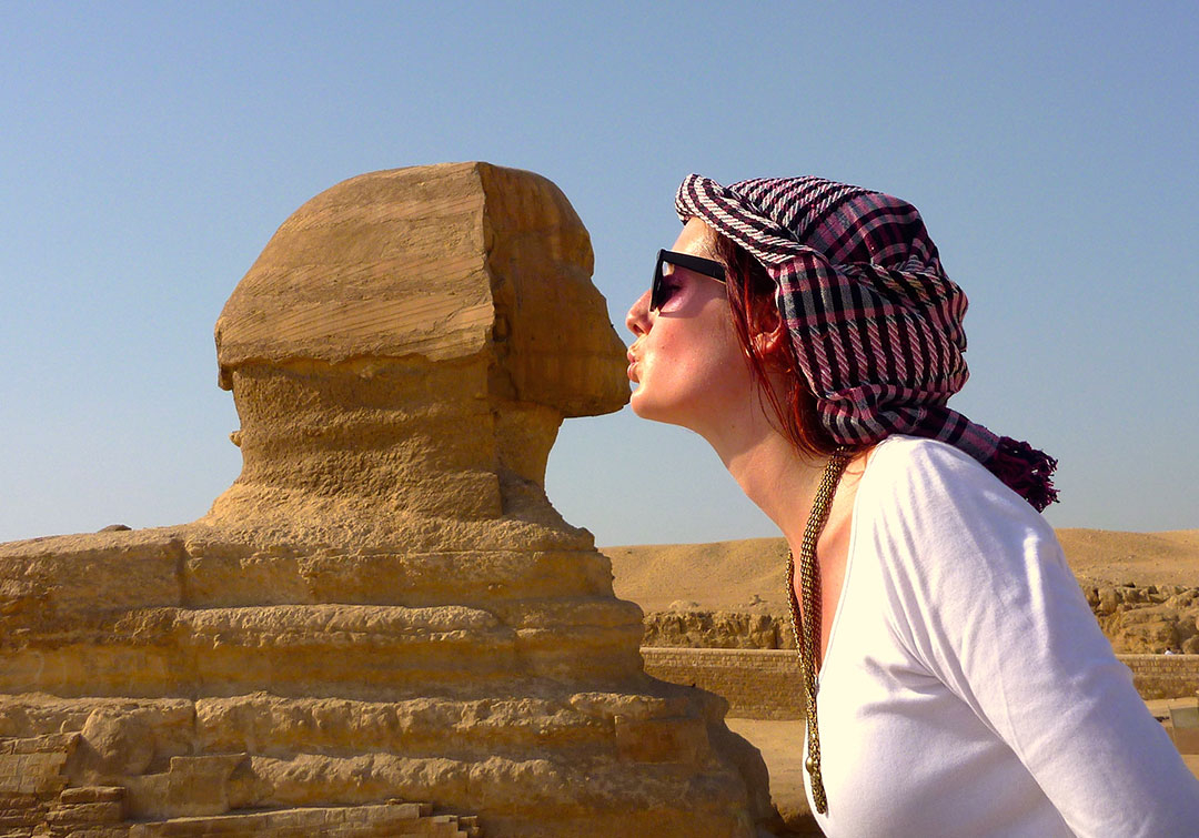 Tacky tourist photo of me pretending to kiss the statue of the Sphinx on a hot summer day while wearing a pink head dress and sunglasses