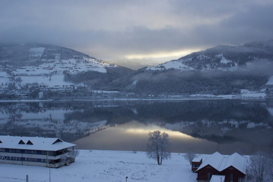 Amazing clear mountain reflections on the lake in Voss, Norway surrounded by snow during winter with the building I slept in for the night in the foreground to the left
