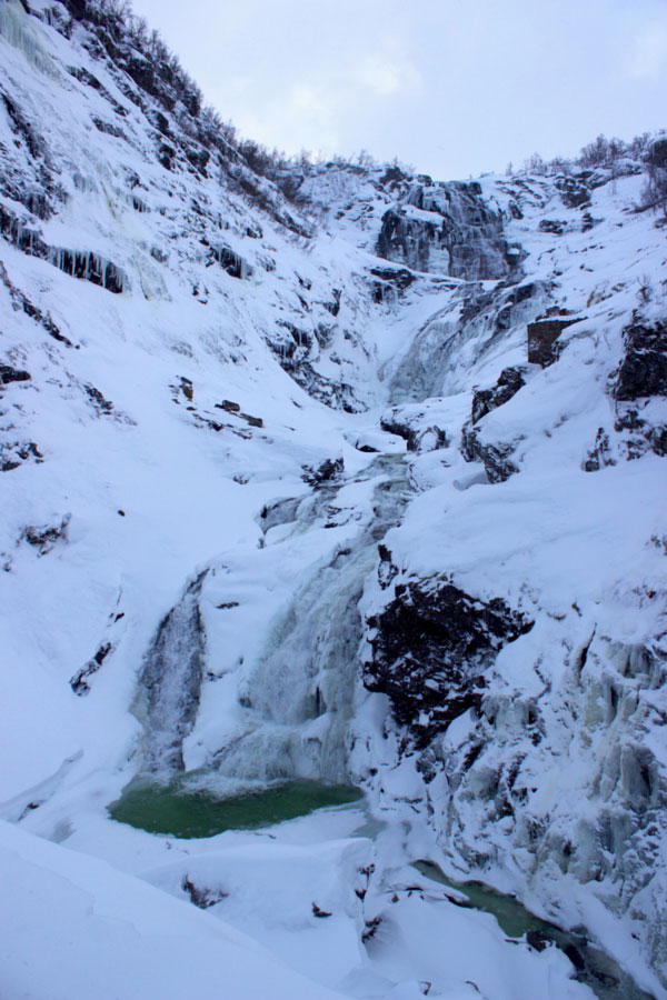 Looking up at Kjosfossen Waterfall covered in snow and partially frozen during winter in Norway on the Norway in a Nutshell self-guided tour