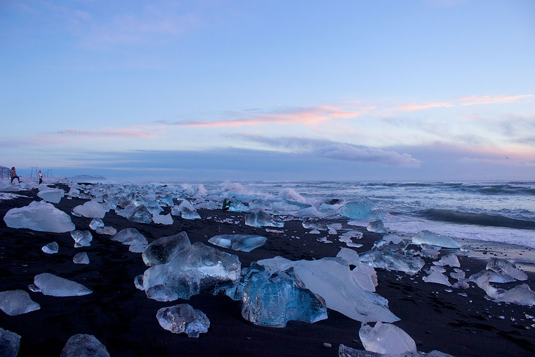 Diamond Beach at Jokulsarlon Glacier Lagoon at sunrise with tiny people standing among icebergs