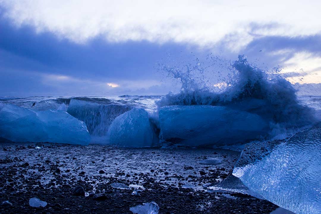 Waves crashing over icebergs on the black sand of Diamond Beach at Jokulsarlon Glacier Lagoon at sunrise